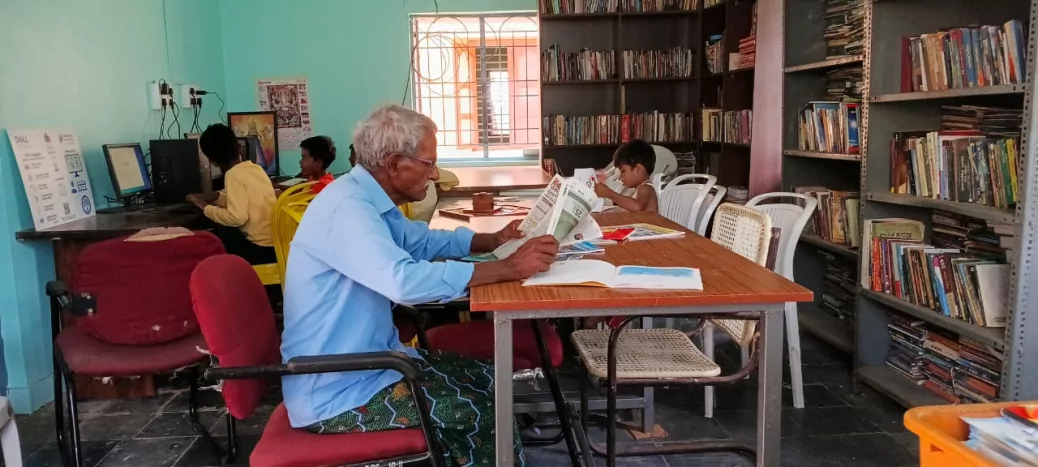 Children and an elder reading together at a gram panchayat library in Karnataka
